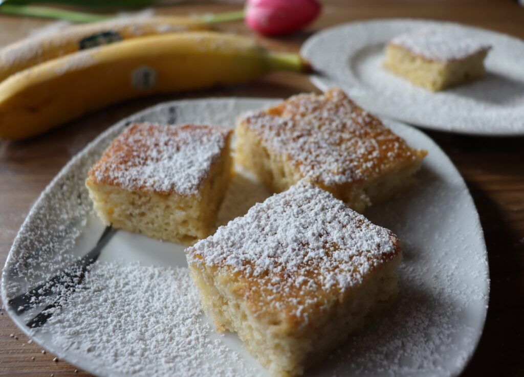 3 Stücke Blechkuchen mit Banane mit Puderzucker bestreut auf einem Teller